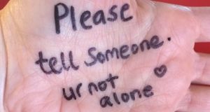 Message in felt tip on open palm: Tell someone. You are not alone.