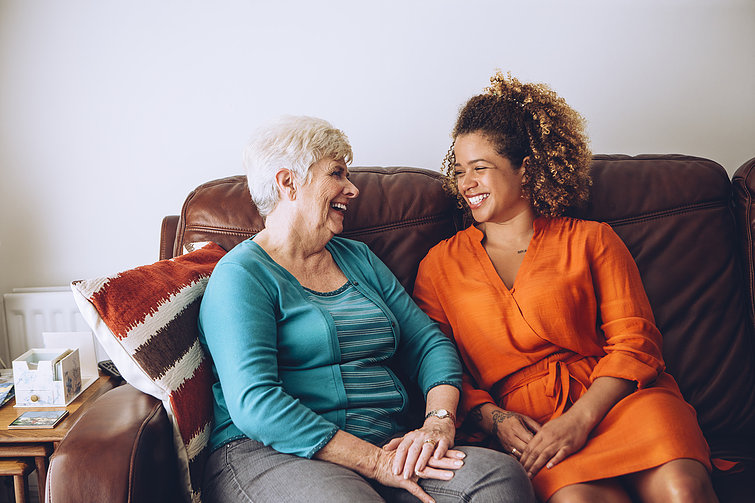 Elderly lady and young homesharer laugh and chat on the sofa