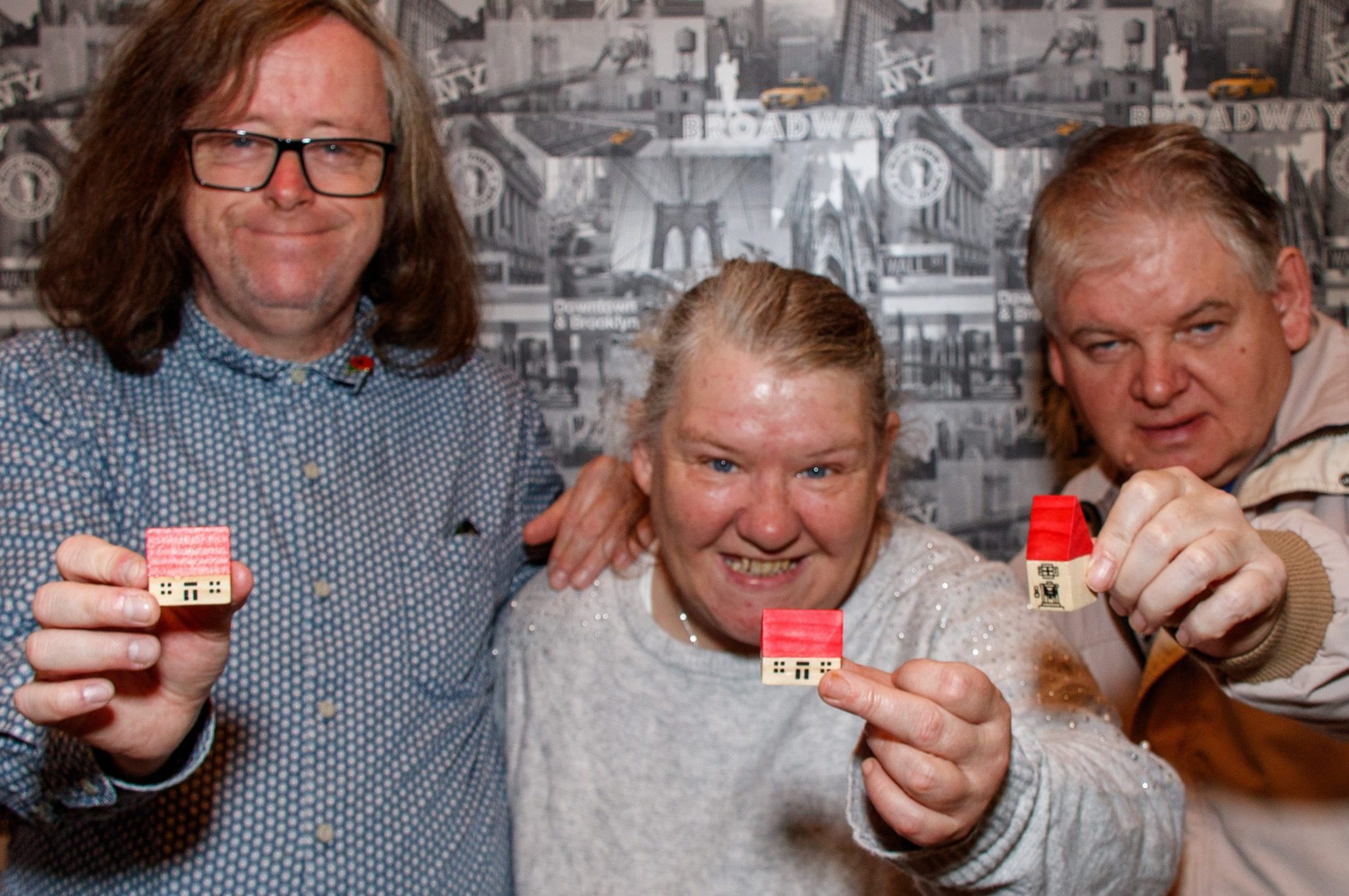 Three people holding models of buildings signifying community