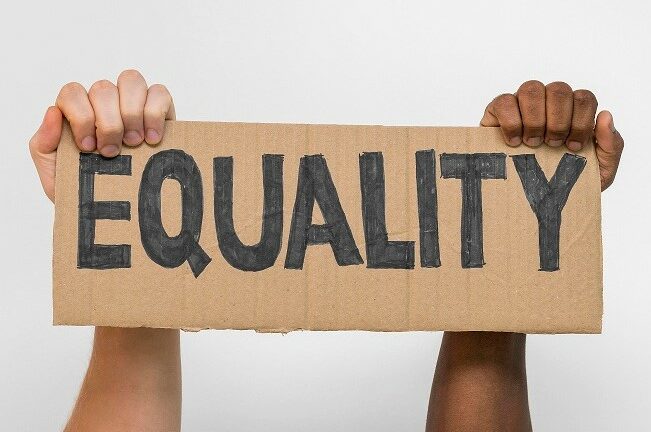Black and white hands holding up a sign with the word 'equality'.