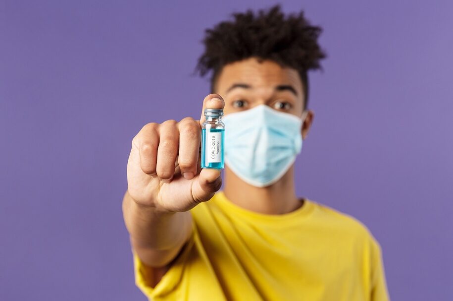 Young man in mask holding vaccine bottle