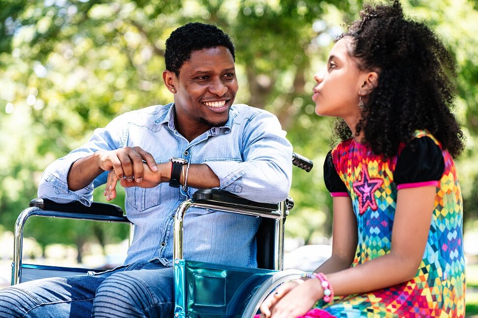 Man in a wheelchair enjoying and having fun with his daughter at the park.