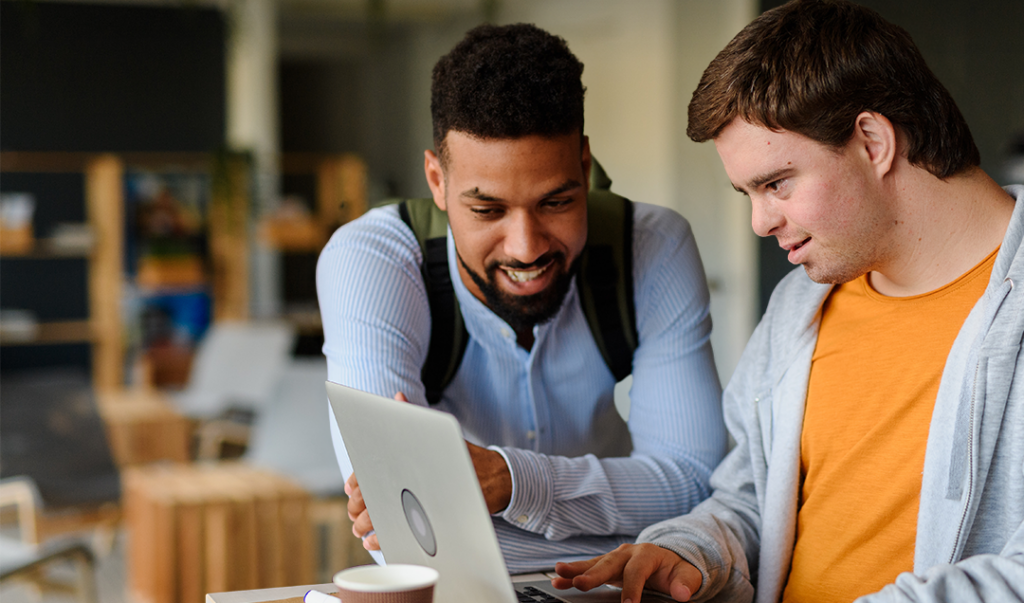 Image shows a young man using a laptop with his carer.